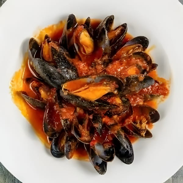 Steamed mussels in a rich red tomato sauce, served on a white plate at Sage Restaurant.