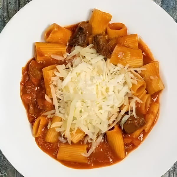 Rigatoni pasta with meat sauce and shredded parmesan cheese on a white plate.