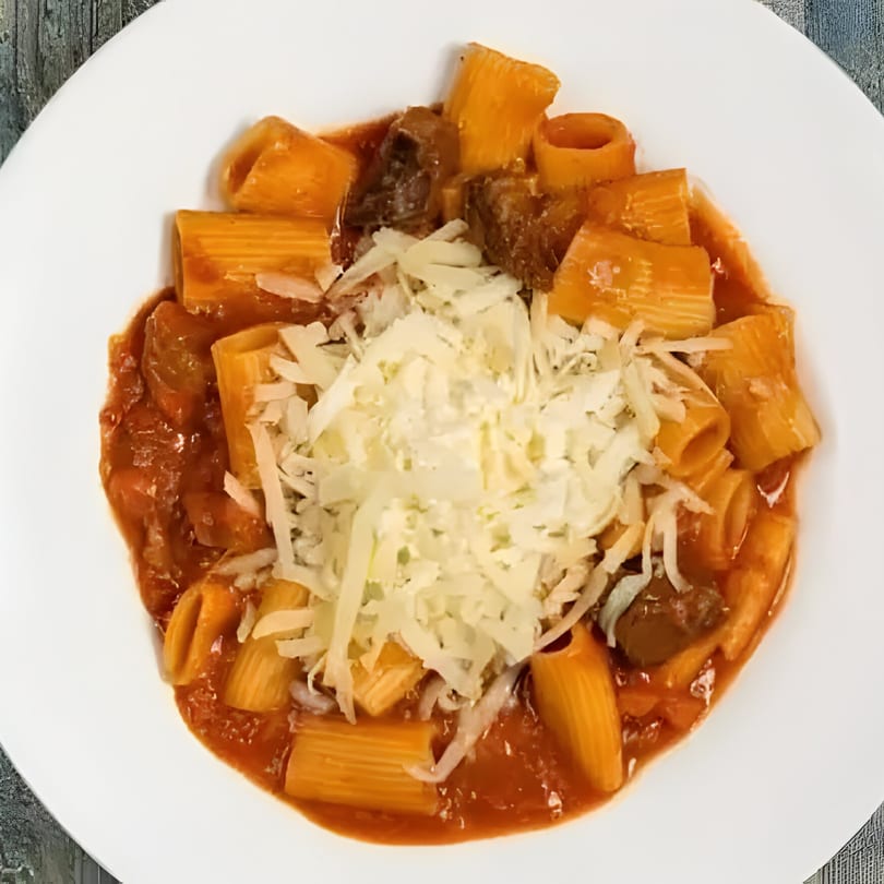 Rigatoni pasta with meat sauce and shredded parmesan cheese on a white plate.