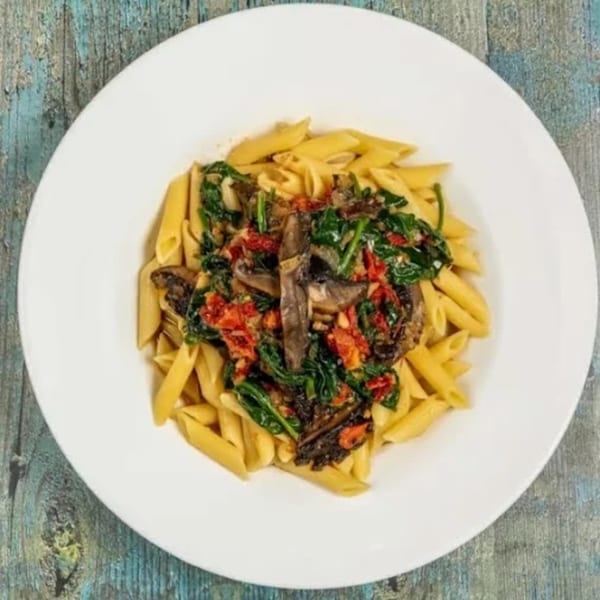 Penne pasta with spinach, sun-dried tomatoes, and mushrooms on a white plate.