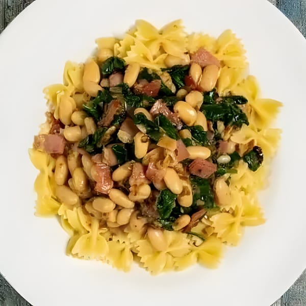 Sage Restaurant's farfalle pasta with white beans, diced ham, and green vegetables on a white plate.